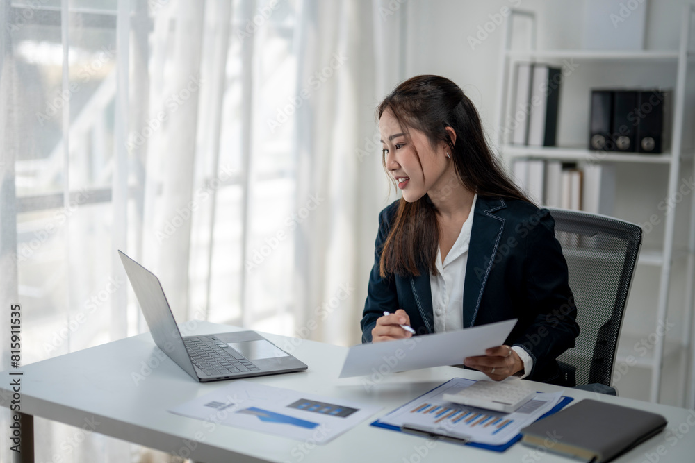 A woman is sitting at a desk with a laptop and a stack of papers. She is smiling and she is enjoying her work. The scene suggests a positive and productive atmosphere in the office A woman is sitting at a desk with a laptop and a stack of papers. She is smiling and she is enjoying her work. The scene suggests a positive and productive atmosphere in the office