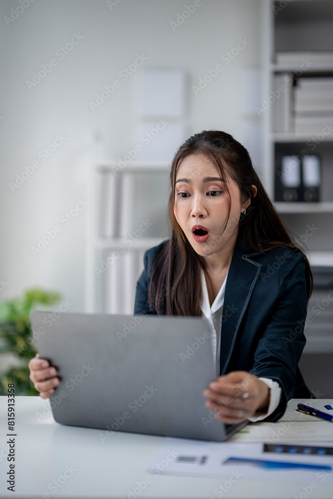 A woman in a business suit is looking at a laptop screen with an open mouth. She is surprised or shocked by something she has seen on the screen A woman in a business suit is looking at a laptop screen with an open mouth. She is surprised or shocked by something she has seen on the screen