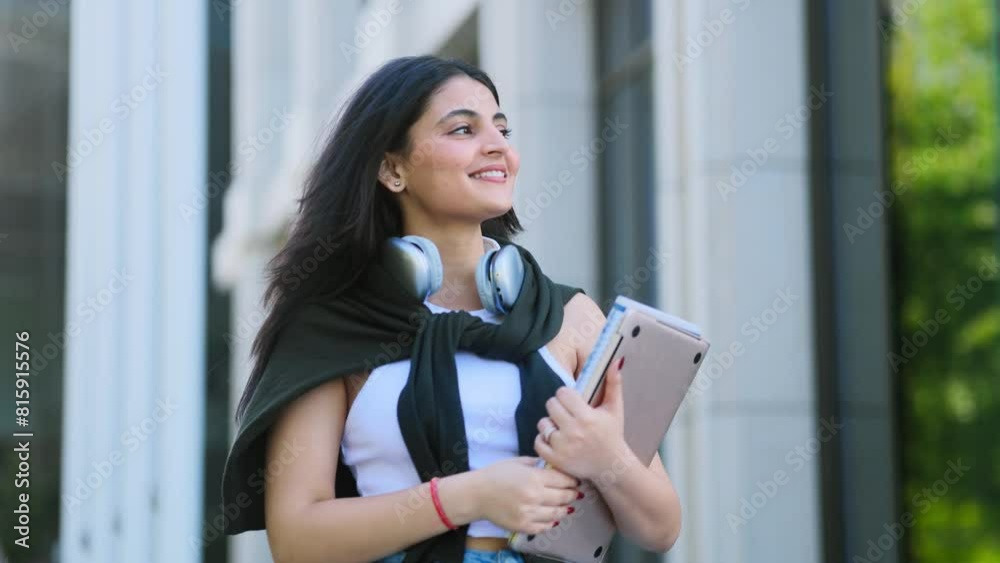 Beautiful brunette indian girl student with notebooks walking down at urban city street after lessons in university and looking around outdoors Successful student concept. High quality 4k footage
