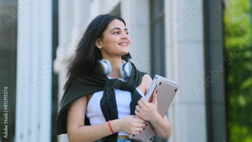 Beautiful brunette indian girl student with notebooks walking down at urban city street after lessons in university and looking around outdoors Successful student concept. High quality 4k footage