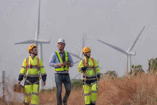 Team maintenance engineer standing discuss against turbines on wind turbine farm.	