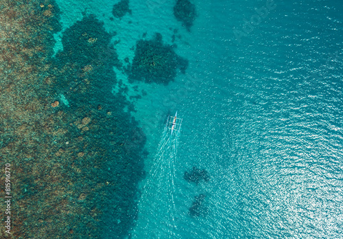 Aerial top view of Banca boat floating in open sea with clear and turquoise water on sunny day . Tropical landscape. Philippines, Palawan.