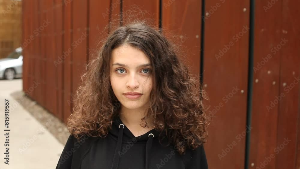 White brunette teenage girl with curly hair poses on the street in the city. White brunette teenage girl with curly hair poses on the street in the city.