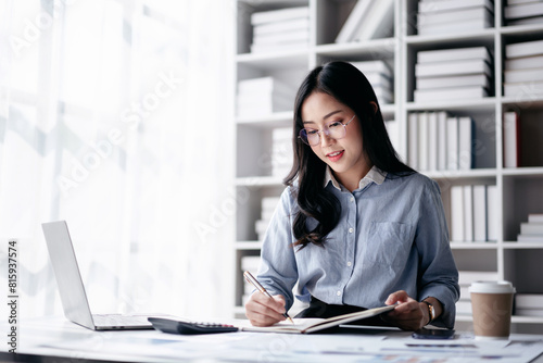 Accounting business concept, Accountant woman reading finance chart on laptop with paperwork and writing