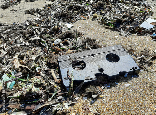 Discarded VHS tape on a littered beach, reflecting the enduring impact of plastic waste. This image captures a slice of the past entangled in today’s environmental challenges.