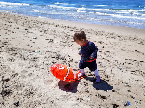 Young child discovers a deflated balloon on the beach. A poignant reminder of the environmental impact of plastic waste on our oceans, depicted through a child's interaction.