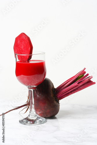 A glass with beet juice decorated with a slice of beet root, on a marble background....