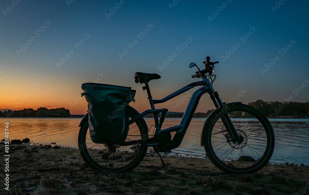 Silhouette of electric bicycle on beach of pond Bezdrev after sunset