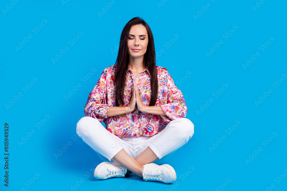 Full length photo of cheerful cute lady dressed print shirt hands arms together sitting legs crossed isolated blue color background Full length photo of cheerful cute lady dressed print shirt hands arms together sitting legs crossed isolated blue color background