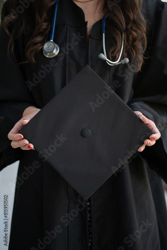 Nursing School Graduate holding cap and gown wearing stethoscope holding cap