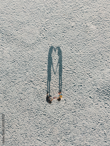 A lovely couple holding hands creates a heart-shaped shadow, captured from a top-down drone view.
