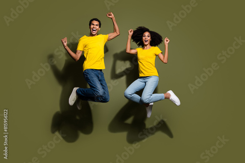Full body portrait of two nice people raise fists jump wear t-shirt isolated on khaki color background © deagreez