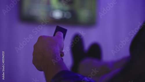 Man sitting on sofa and watching TV with remote controller in his hand