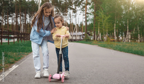 Family care concept. A little girl teaches her sister to ride a scooter in the park.