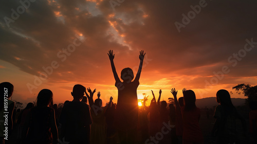 Silhouette of a refugee kid group playing at sunset, back view with raised hands in worship and prayer, symbolizing hope, freedom, and diverse faith. Captured during World Refugee Day, portraying © Spear