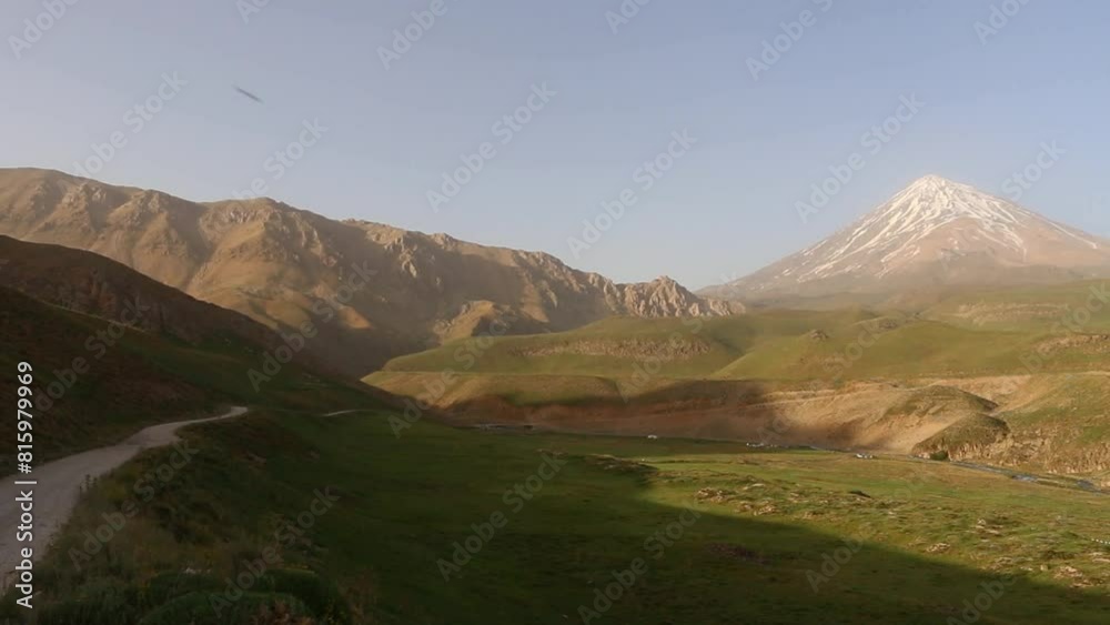 majestic Damavand mountain, showing a light dusting of snow as a flock of sheep peacefully graze on the lush plain. majestic Damavand mountain, showing a light dusting of snow as a flock of sheep peacefully graze on the lush plain.