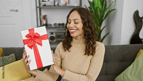 Cheery and confident young african american woman elatedly clutching her birthday gift, showcasing her toothy smile in the cozy interior of her home. photo