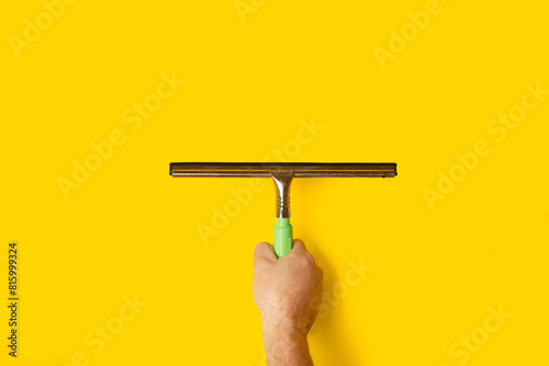 Mano sosteniendo un secador para vidrios sobre un fondo amarillo. Vista de frente y de cerca. Copy space
