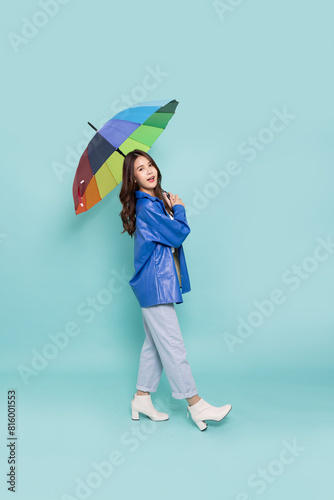 Young Asian woman wearing raincoat and holding rainbow umbrella isolated on green background, In the rainy season concept