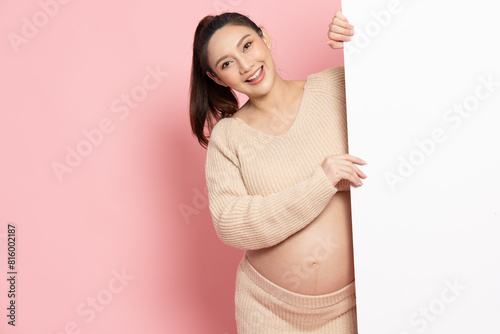Asian pregnant woman is standing behind the white blank banner to empty copy space advertisement board, Looking at camera