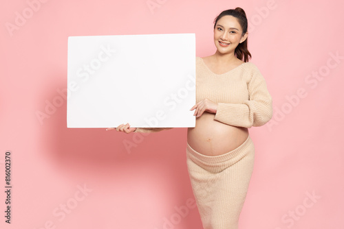 Asian pregnant woman showing and holding blank white billboard isolated on pink background