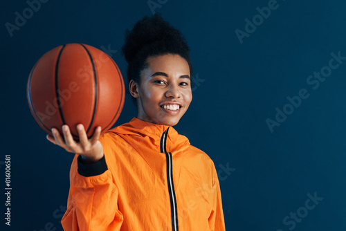 Portrait of a young woman holding a basketball in her hand. Female basketball player in orange sportswear looking at camera.