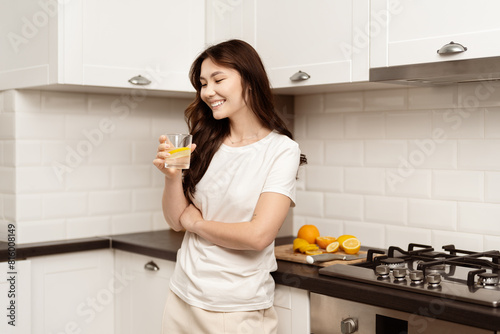 Happy Woman Enjoying Fresh Lemon Water In Modern Kitchen With White Cabinets. Captures Healthy Lifestyle And Positive Morning Routine. Bright  Clean  And Fresh Aesthetic.