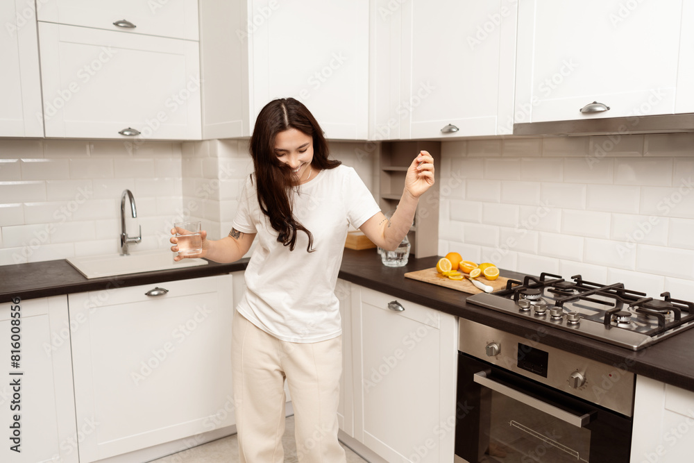 Woman Dancing In Kitchen With Glass Of Water And Sliced Lemons, Joyful Home Life, Healthy Lifestyle, Modern Kitchen Interior Woman Dancing In Kitchen With Glass Of Water And Sliced Lemons, Joyful Home Life, Healthy Lifestyle, Modern Kitchen Interior