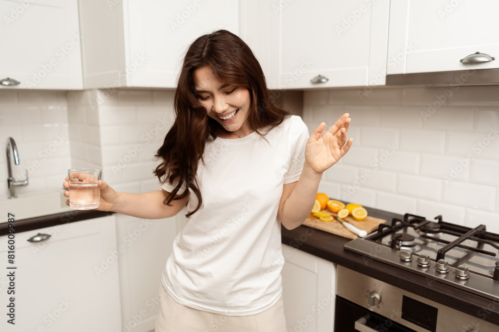 Happy Young Woman Enjoying Music and Dancing In Modern Kitchen With Healthy Fruit And Water Setup, Casual Style Home Indoor Happiness