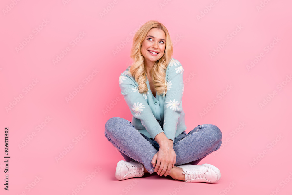 Full size photo of lovely woman sit floor crossed legs empty space dressed stylish flower print garment isolated on pink color background Full size photo of lovely woman sit floor crossed legs empty space dressed stylish flower print garment isolated on pink color background