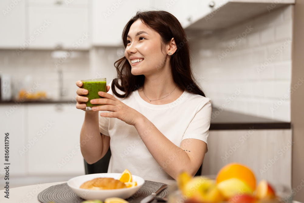 Young Woman Enjoying Healthy Breakfast, Smiling And Holding A Green Smoothie In A Modern Kitchen, Wellness And Healthy Lifestyle Concept Young Woman Enjoying Healthy Breakfast, Smiling And Holding A Green Smoothie In A Modern Kitchen, Wellness And Healthy Lifestyle Concept