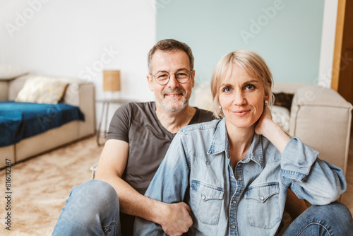 Smiling middle-aged couple sitting together in a cozy living room, enjoying quality time. Happy and relaxed, they are spending leisure time at home.