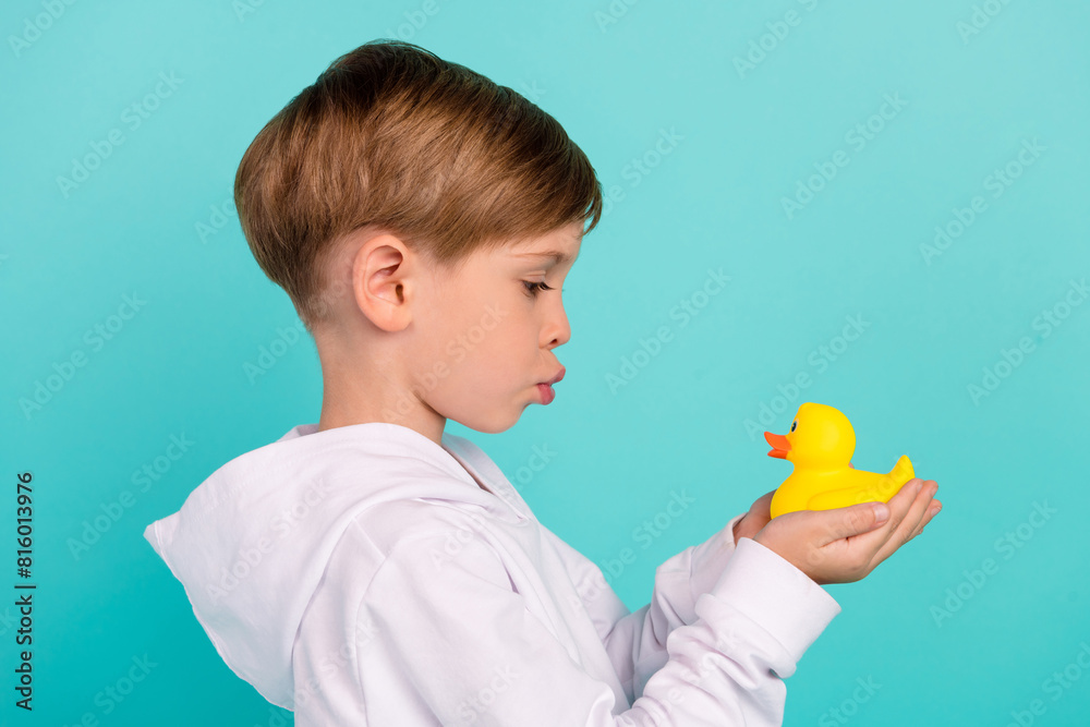 Profile side photo of sweet adorable kid boy playing with yellow rubber duck game isolated cyan color background Profile side photo of sweet adorable kid boy playing with yellow rubber duck game isolated cyan color background