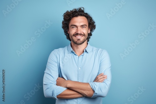 Portrait of a cheerful man in his 30s with arms crossed while standing against soft blue background photo