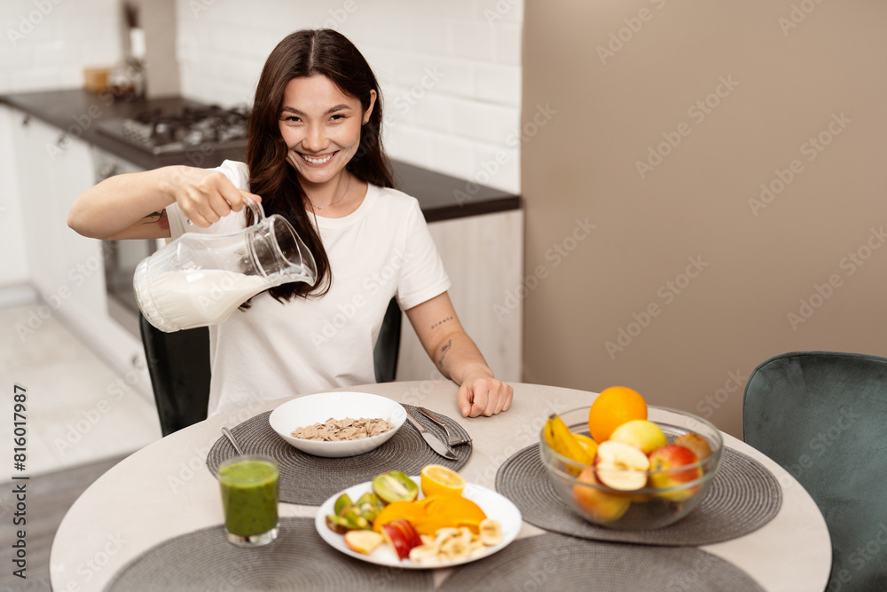 Happy Woman Pouring Milk Into Cereal In Bright Kitchen, Healthy Breakfast, Smiling, Lifestyle, Modern Interior. Concept Of Joyful Daily Routine And Healthy Eating Habits. Happy Woman Pouring Milk Into Cereal In Bright Kitchen, Healthy Breakfast, Smiling, Lifestyle, Modern Interior. Concept Of Joyful Daily Routine And Healthy Eating Habits.