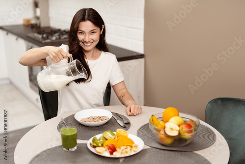 Happy Woman Pouring Milk Into Cereal In Bright Kitchen, Healthy Breakfast, Smiling, Lifestyle, Modern Interior. Concept Of Joyful Daily Routine And Healthy Eating Habits.