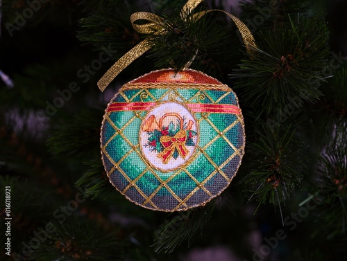 A cross stitched Christmas Timeless Elegance ornament on to a Christmas tree. This green Christmas ornament with horn, plant and bow embroidered and made by myself.