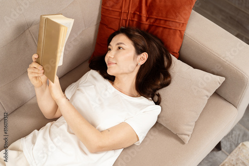 Young Woman Relaxing On Sofa With Book, Enjoying Her Leisure Time At Home, Peaceful And Content