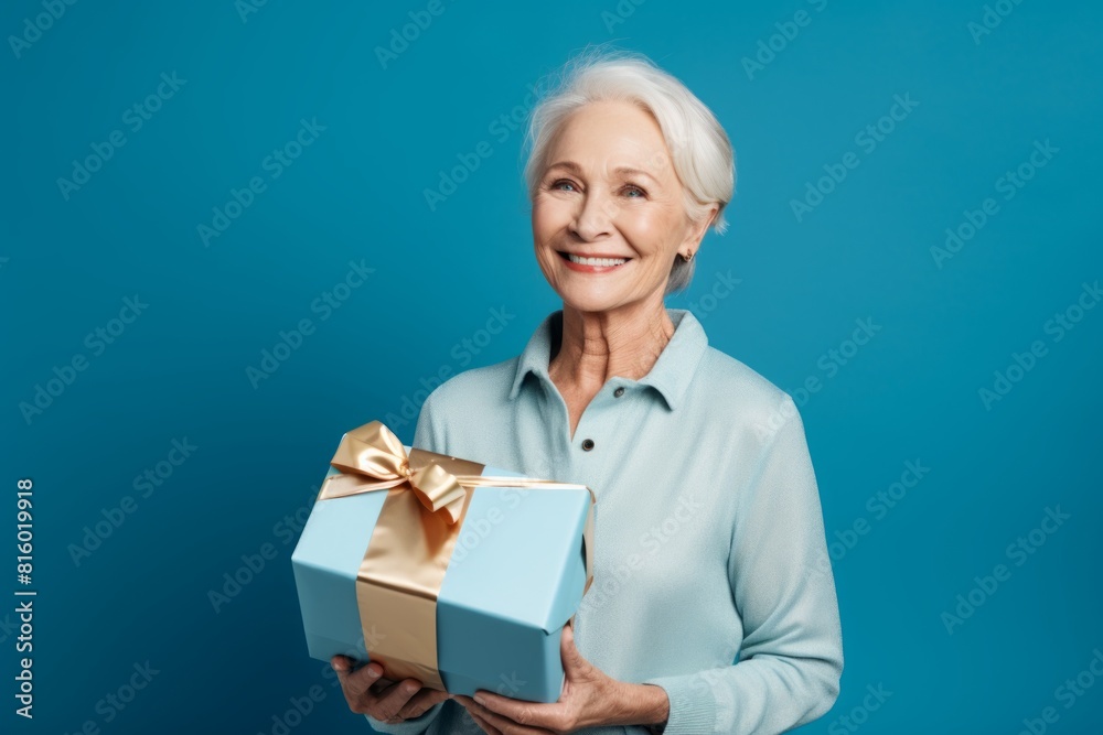Portrait of a glad woman in her 60s holding a box while standing against soft blue background Portrait of a glad woman in her 60s holding a box while standing against soft blue background