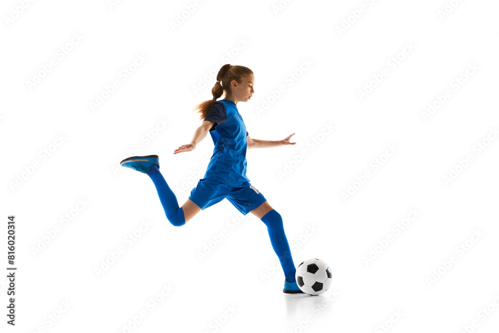Dynamic image of teen girl, football player in blue uniform training, in motion with ball isolated on white studio background. Concept of sport, active and healthy lifestyle, childhood, school, hobby