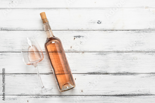Flat lay bottle and glass with rose wine, white wooden background. View from above.
