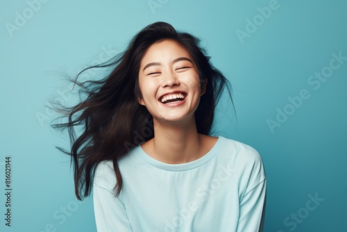 Portrait of a joyful asian woman in her 20s with arms crossed in front of soft blue background