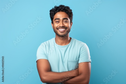 Portrait of a grinning indian man in his 20s with arms crossed over soft blue background photo