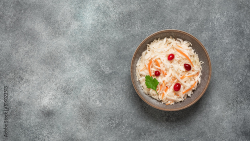 Sauerkraut with cranberries and carrots in a bowl on a gray concrete background. Top view, flat lay, copy space.