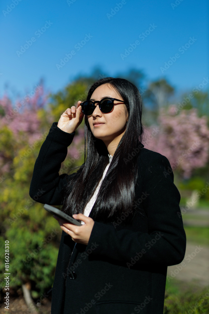 A smart and attractive Korean woman uses her smartphone in the park, radiating happiness and beauty. A smart and attractive Korean woman uses her smartphone in the park, radiating happiness and beauty.