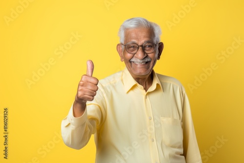 Portrait of a happy indian elderly man in his 90s showing a thumb up isolated on soft yellow background