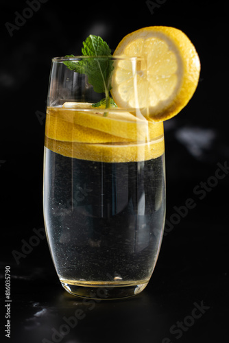 glass of water with lemon,A glass of cold water with lemon pieces on a black background, refreshing lemon water, lemon water