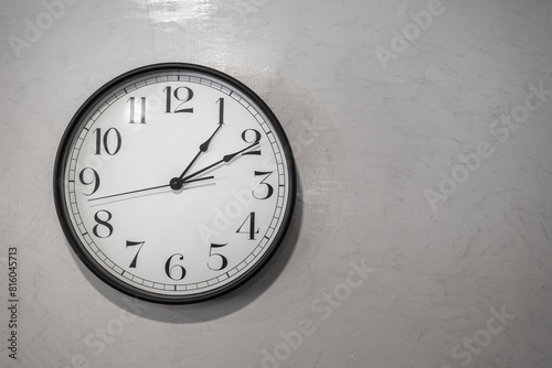 A classic round clock with numbers which is installed on white plain wall. Interior decoration object photo. Close-up and selective focus at some part of the clock.