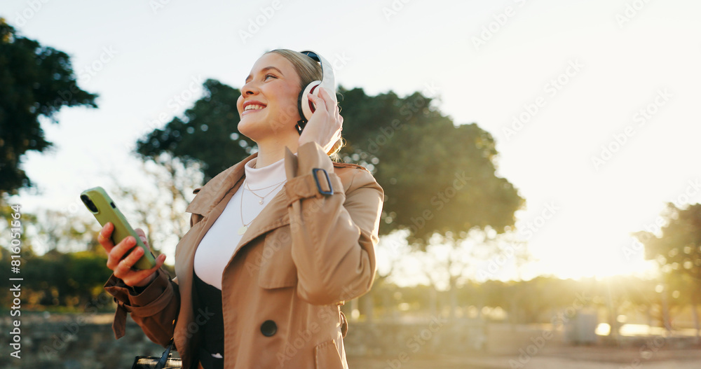 Fototapeta premium Woman, business and headphones with cellphone in park for work commute, streaming or podcast. Female person, walking and happiness in urban city for morning travel with music, entertainment or audio