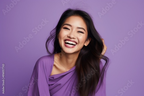 Portrait of a grinning asian woman in her 20s smiling at the camera over soft purple background